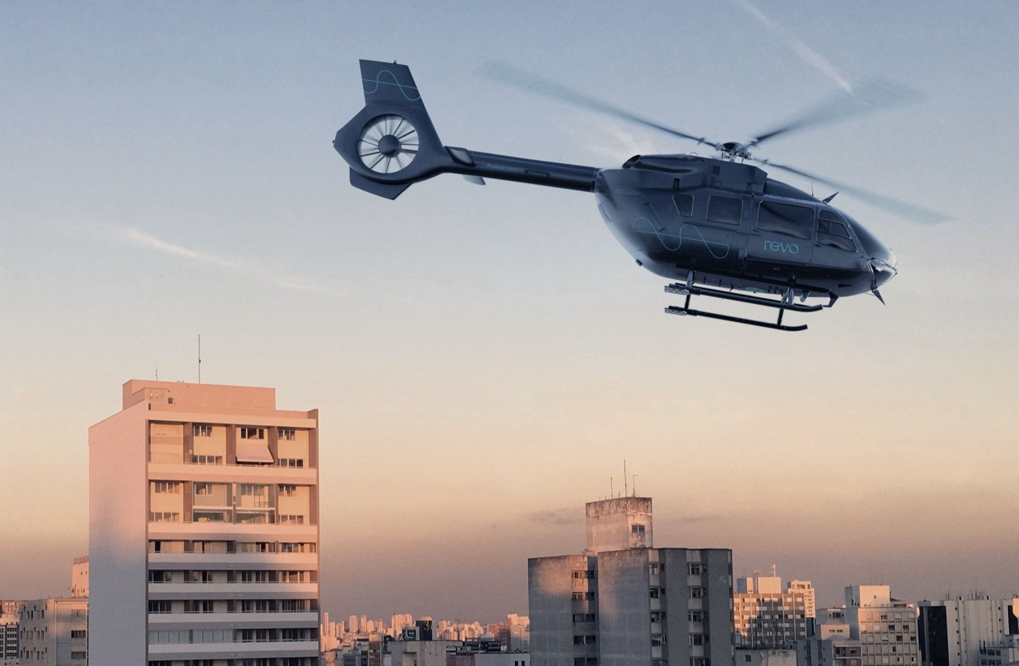 A Revo helicopter lifting away above the city skyline at dusk.